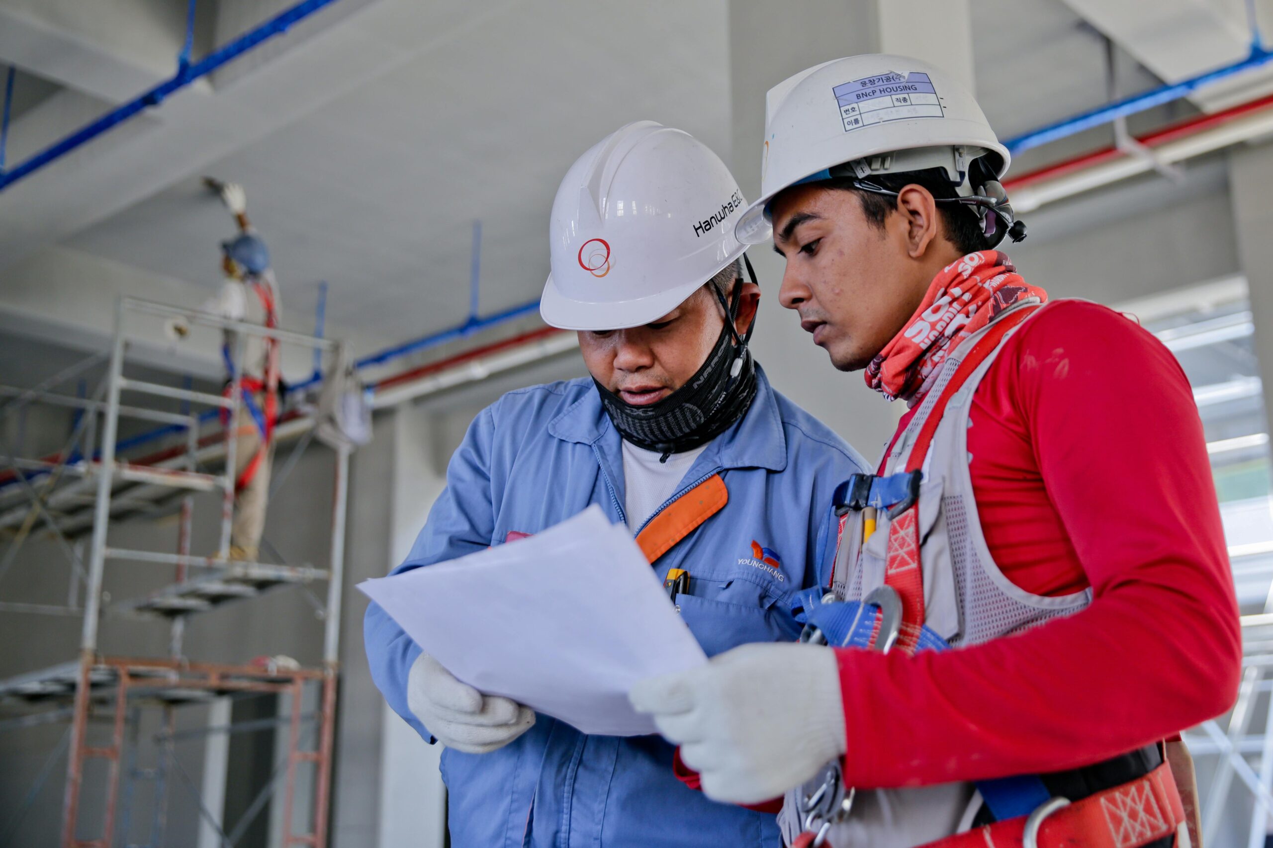 Todos los cursos Two engineers in safety helmets reviewing construction plans at a worksite.